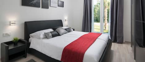 Un dormitorio moderno con una cama grande, una mesita de noche, un plaid rojo y una obra de arte en la pared.