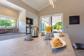 Una cocina moderna con una isla grande, una tetera, un vaso de jugo de naranja y croissants en la encimera.