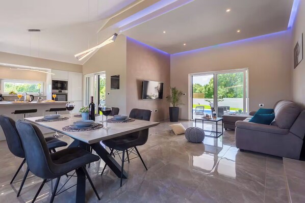 Una cocina moderna con comedor, una sala de estar con sofá y televisión, y un ventanal grande.