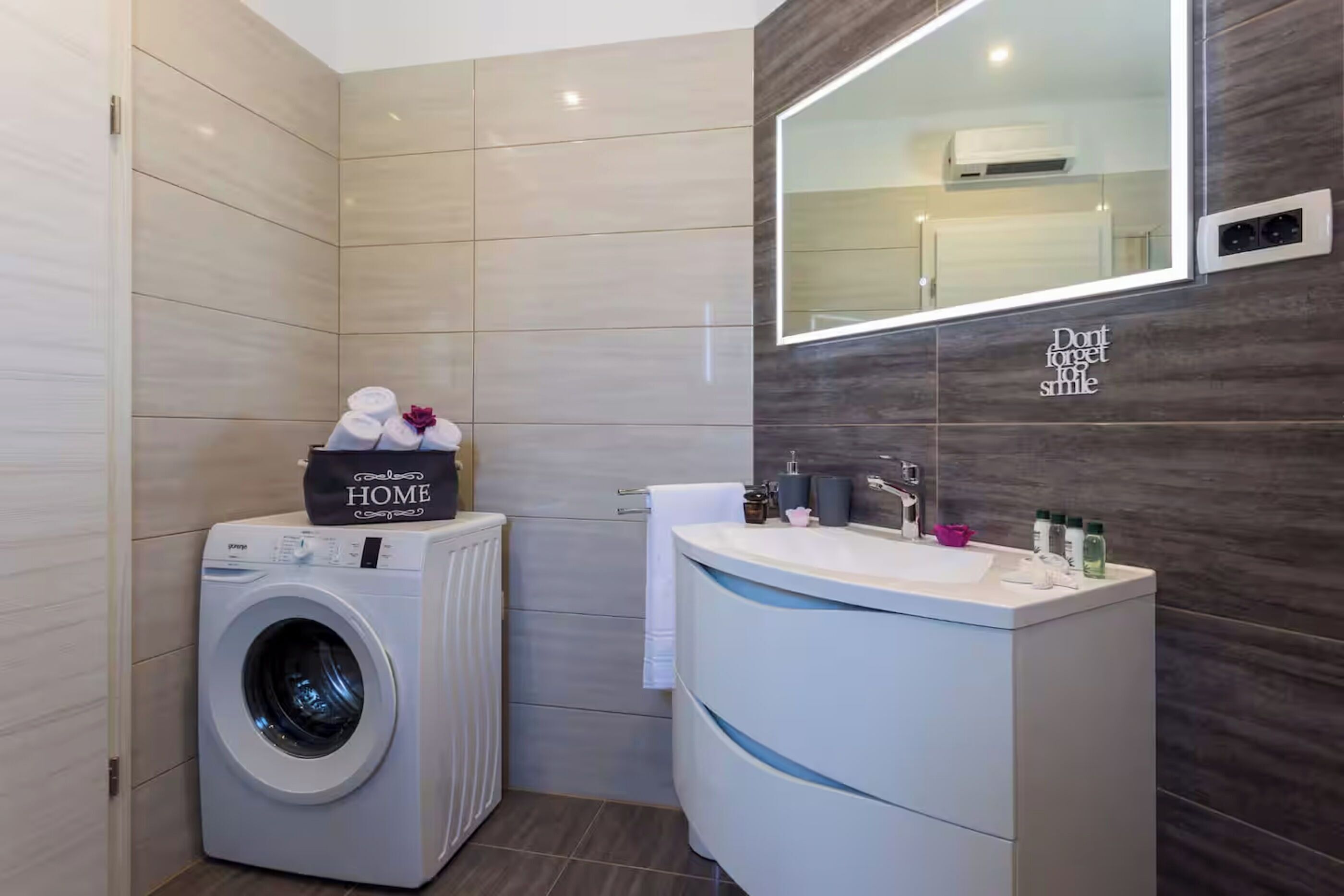 Een moderne badkamer met een ingebouwde wasmachine, een wastafelmeubel met spiegel en een handdoekhouder.
