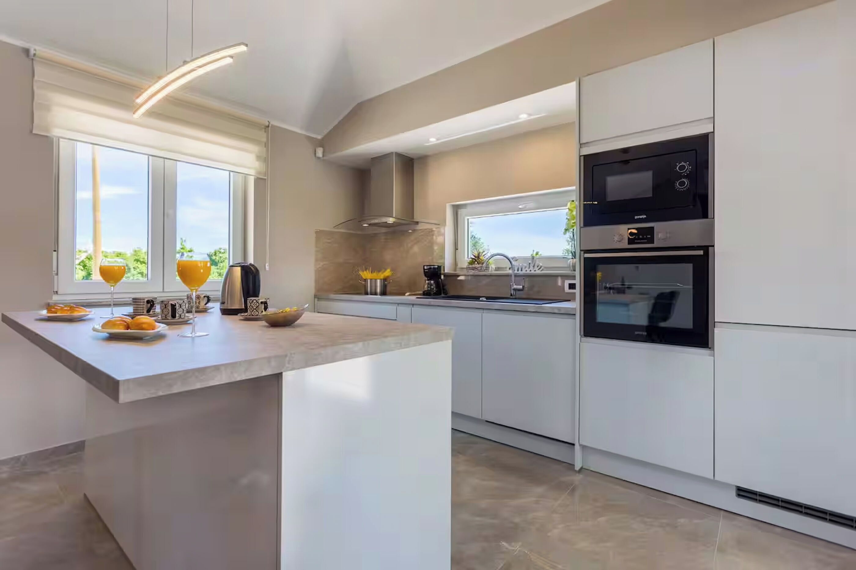 A modern kitchen with a central island, built-in oven, and a large window.