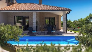 Una casa con piscina, pilares de piedra y techo de tejas.