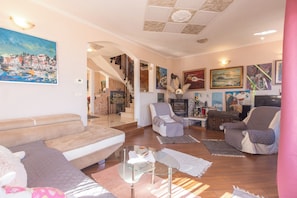 A living room with a sofa, armchairs, a glass coffee table, and artwork on the walls. - Villa Emily (Opatija)