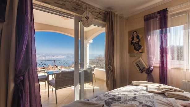 Un dormitorio con cama, ventana con cortinas, vista al exterior y un reloj en la pared.