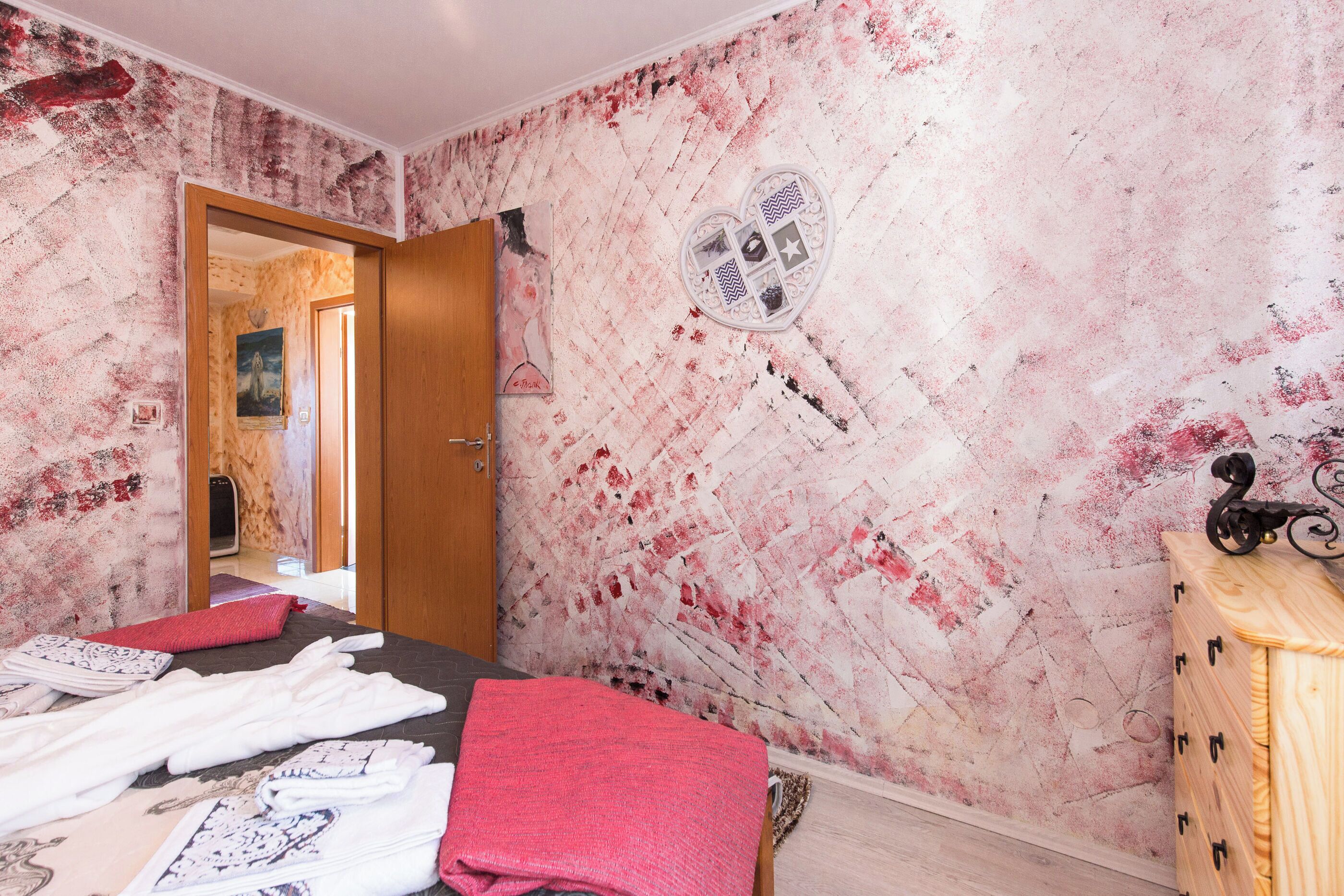 A room with a bed, a wooden dresser, a mirror, and a wall with a textured pattern.