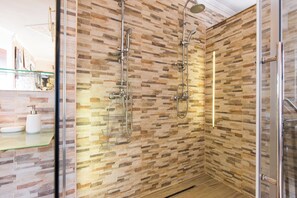 A shower with a glass door, a stone-patterned wall, and a glass shelf with toiletries. - Villa Emily (Opatija)