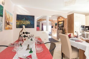 A dining area with a red tablecloth, white table, and various glassware. There are paintings on the walls and a kitchen in the background. - Villa Emily (Opatija)