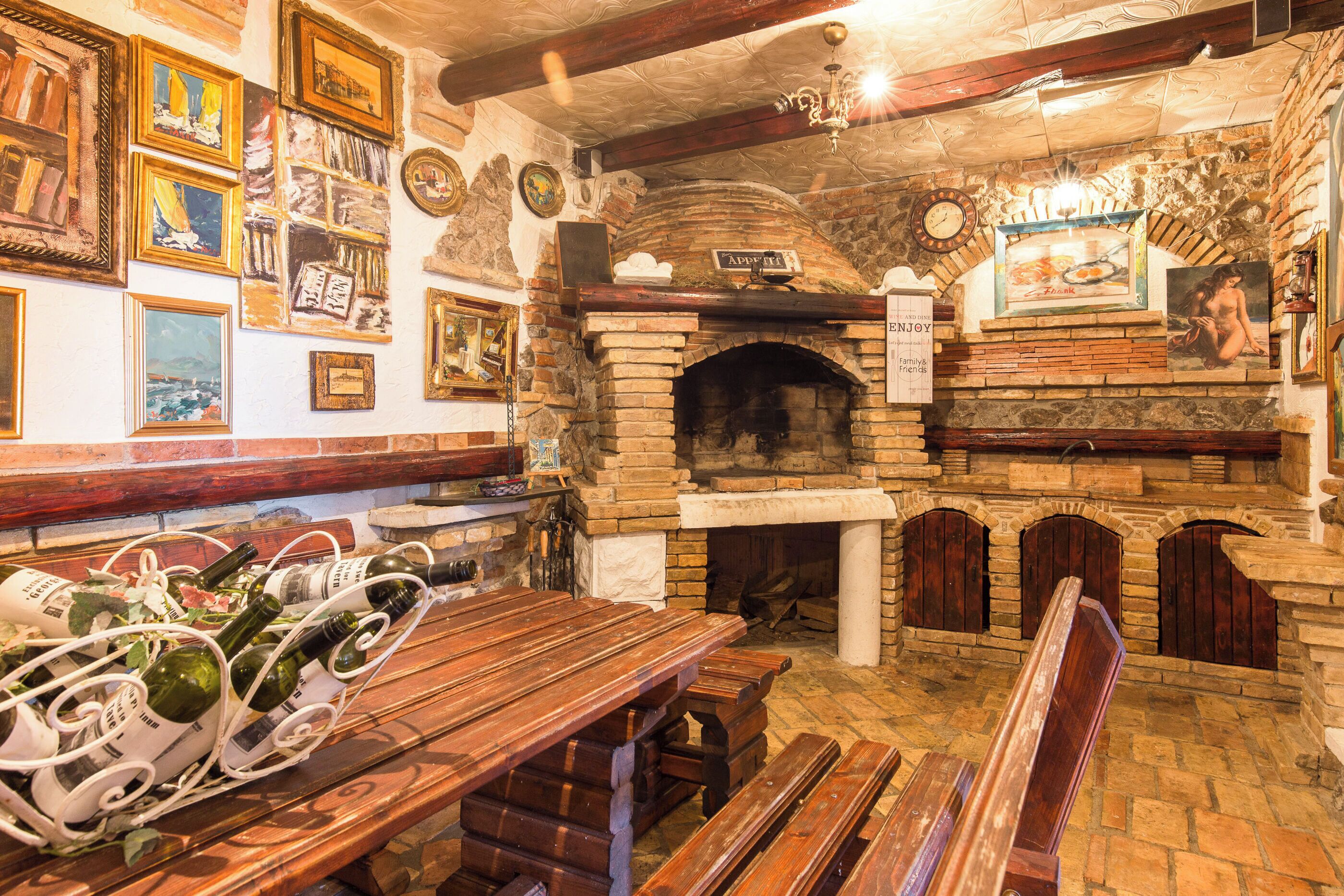 A rustic interior with a stone fireplace, wooden benches, and a wine rack with bottles.