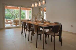 Ein Essbereich mit einem für sechs Personen gedeckten Tisch, umgeben von Stühlen, mit Blick ins Freie durch große Fenster.