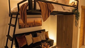Une pièce avec un lit superposé, un canapé, une table basse avec des livres et une bougie, et une échelle.
