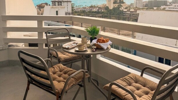 Un balcon avec deux fauteuils confortables, une petite table ronde ornée d’une plante, un croissant et une tasse.