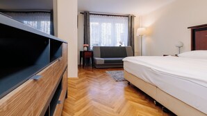 Une chambre d’hôtel avec un lit, une télévision, un canapé, une lampe et une fenêtre avec des rideaux.