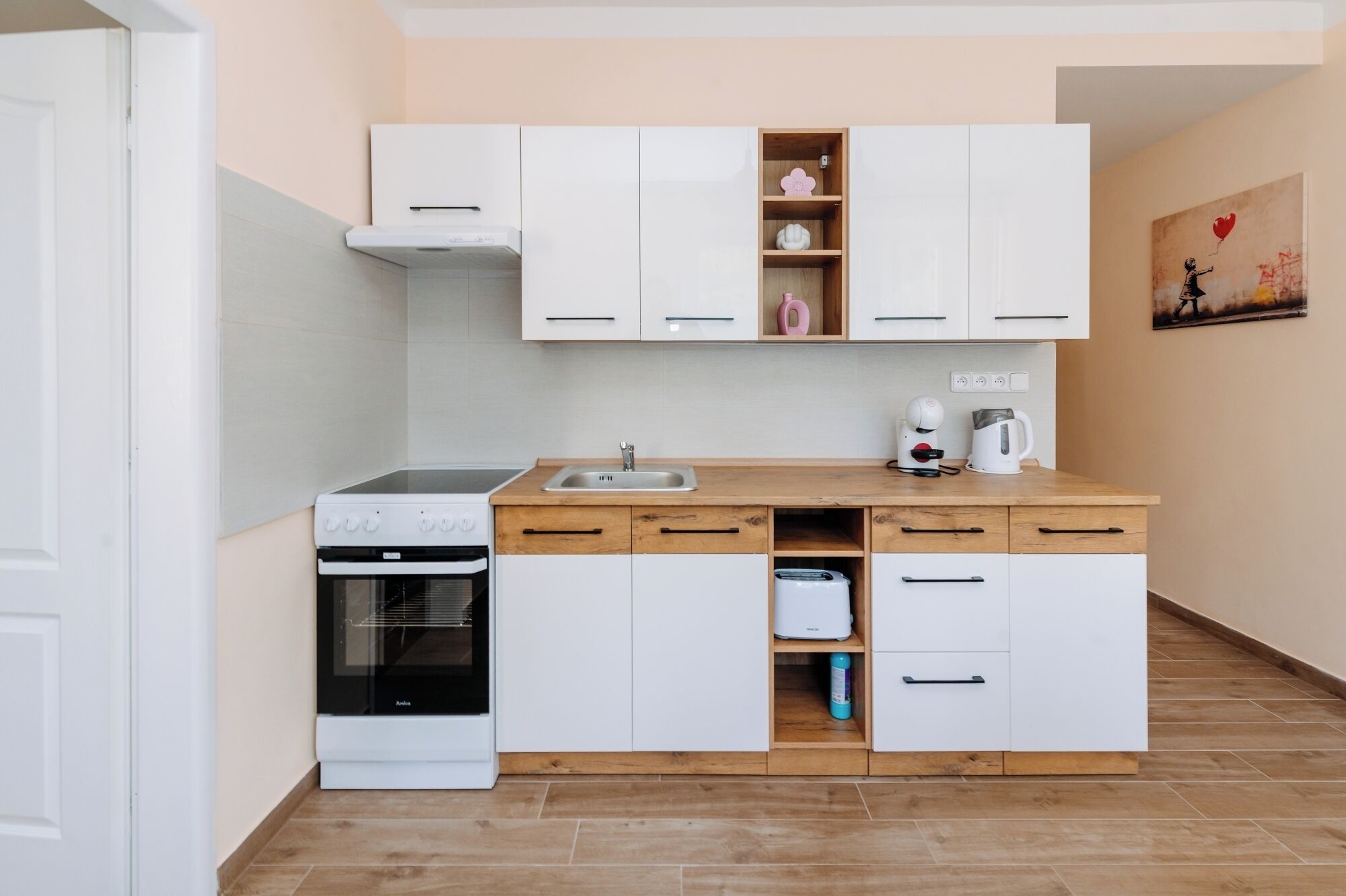 A compact kitchen with white cabinets, a built-in oven, a coffee maker, and a toaster.