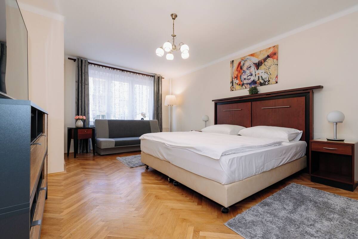 A hotel room with a bed, a desk, a chair, a TV, a window with curtains, and a painting on the wall.