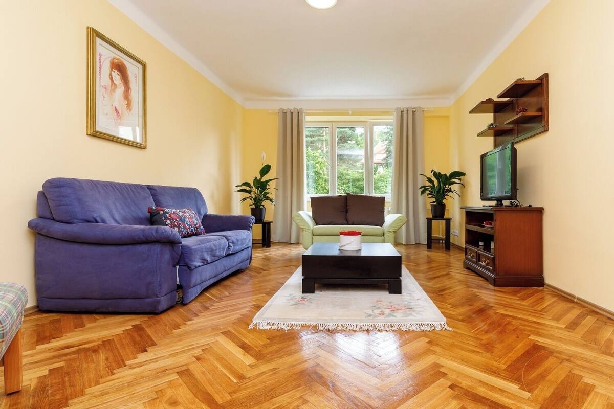 A living room with a sofa, armchair, coffee table, TV stand, and potted plants.