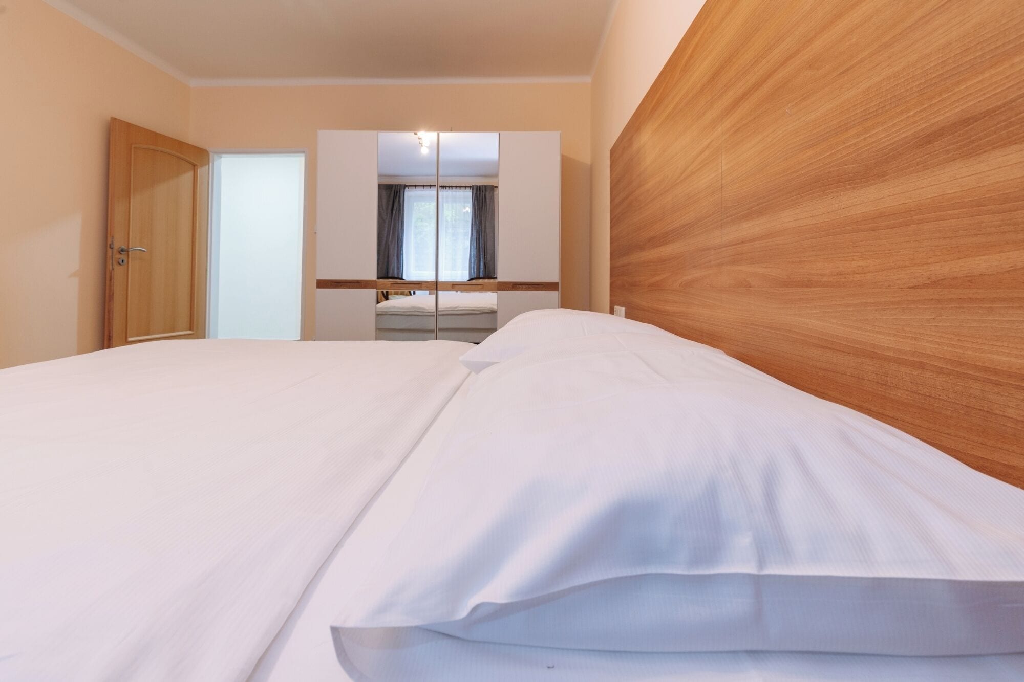 A hotel room with a wooden headboard, a bed with white bedding, a mirror, and a window with curtains.