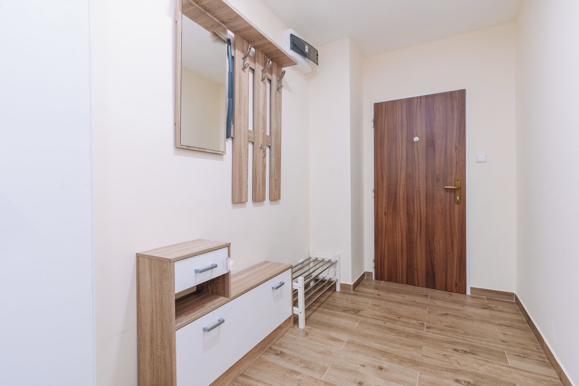 Una stanza con pavimento in legno, un armadio bianco, una porta in legno e uno specchio fissato al muro.