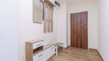 Una stanza con pavimento in legno, un armadio bianco, una porta in legno e uno specchio fissato al muro.