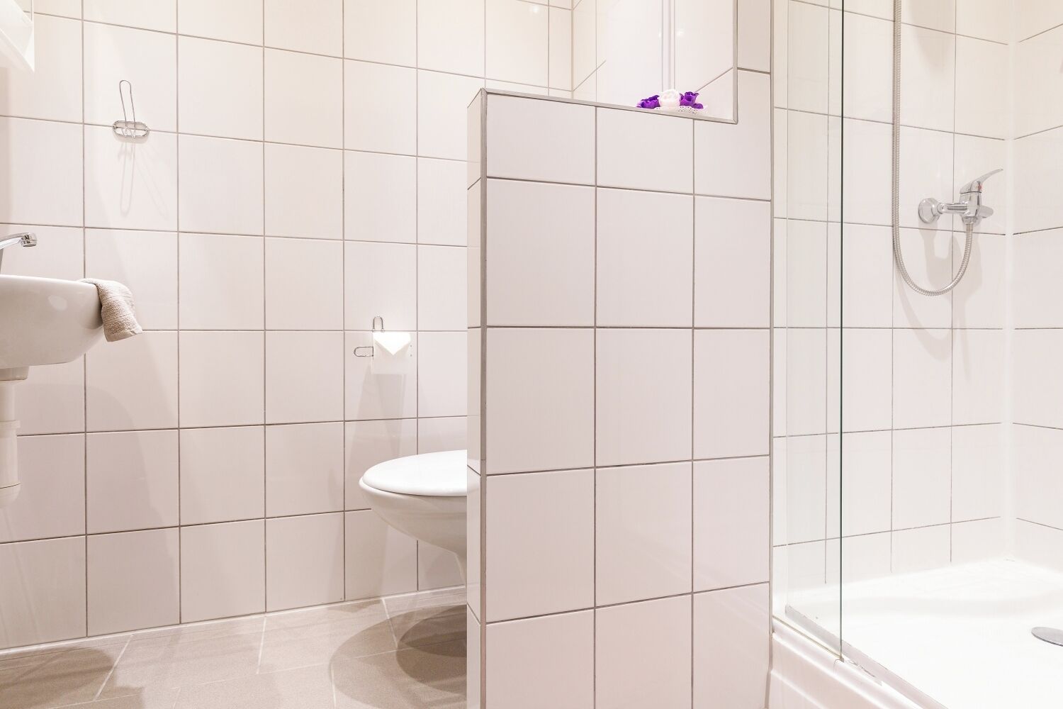 A bathroom with white tiles, a toilet, a shower area, and a towel rack.