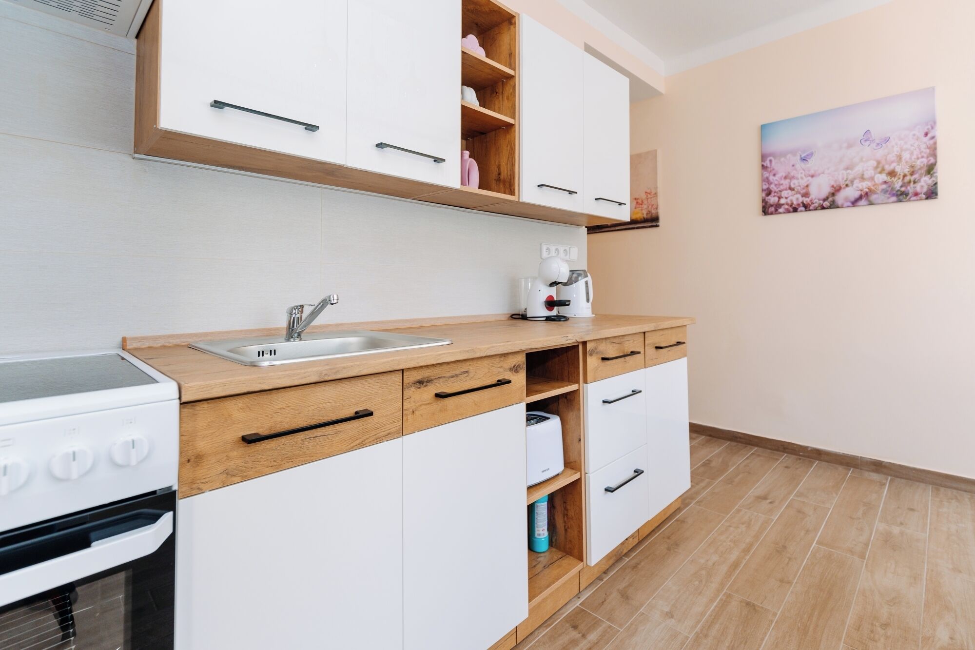 Una cucina compatta con lavello, piano cottura e pensili bianchi.