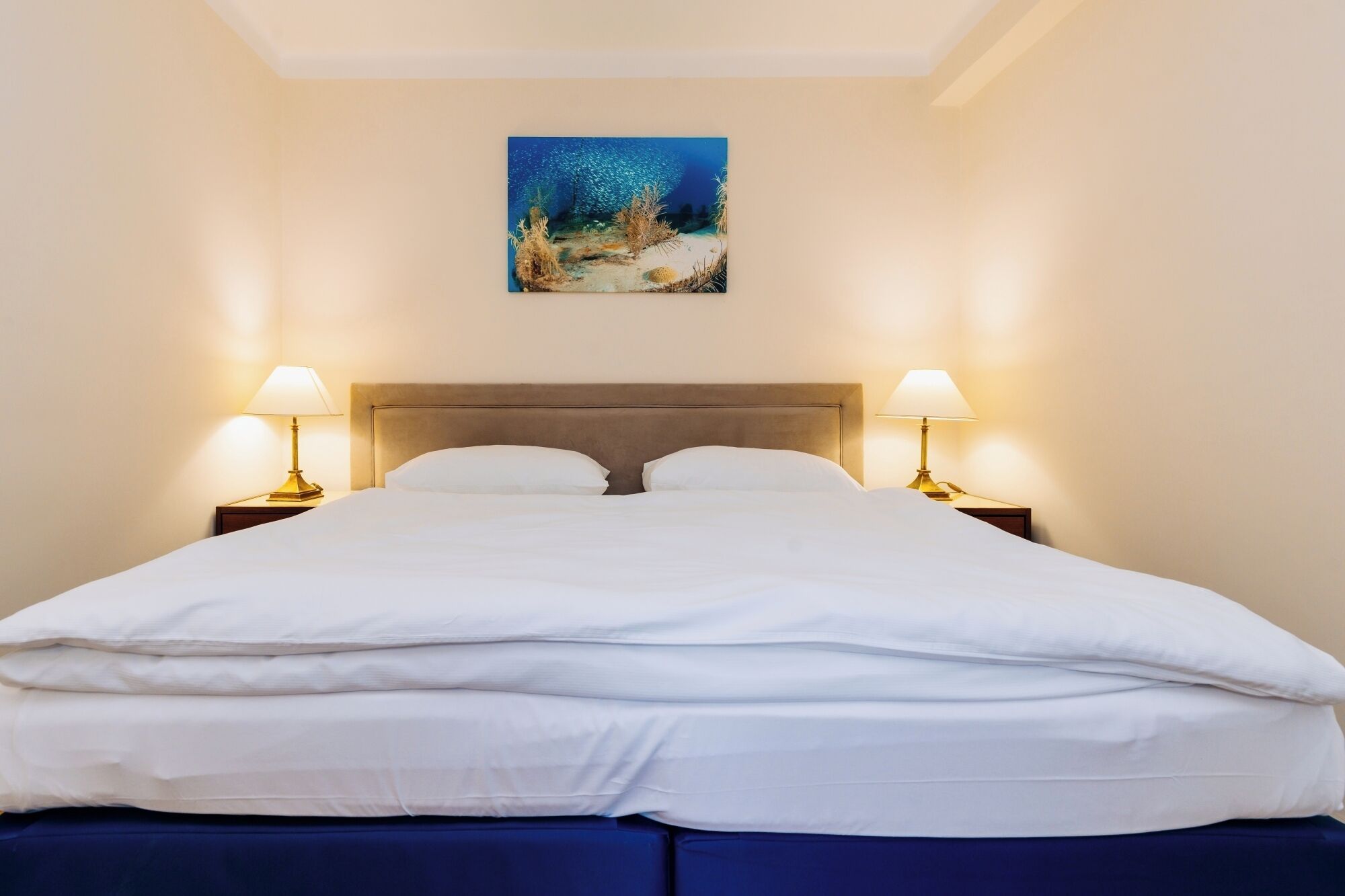 A hotel room with a bed, two bedside lamps, and a painting above the bed.