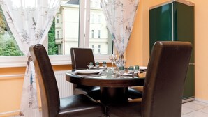 Un coin repas avec une table dressée pour deux personnes, une fenêtre avec des rideaux et un réfrigérateur vert.