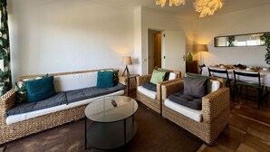 A living room with wicker furniture, a round coffee table, and a dining area with a table set for four. - Praia DA Rocha Twins 5 by Homing (Portimão)