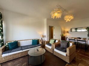 A living room with wicker furniture, a round coffee table, and a dining area with a table set for four. - Praia DA Rocha Twins 5 by Homing (Portimão)