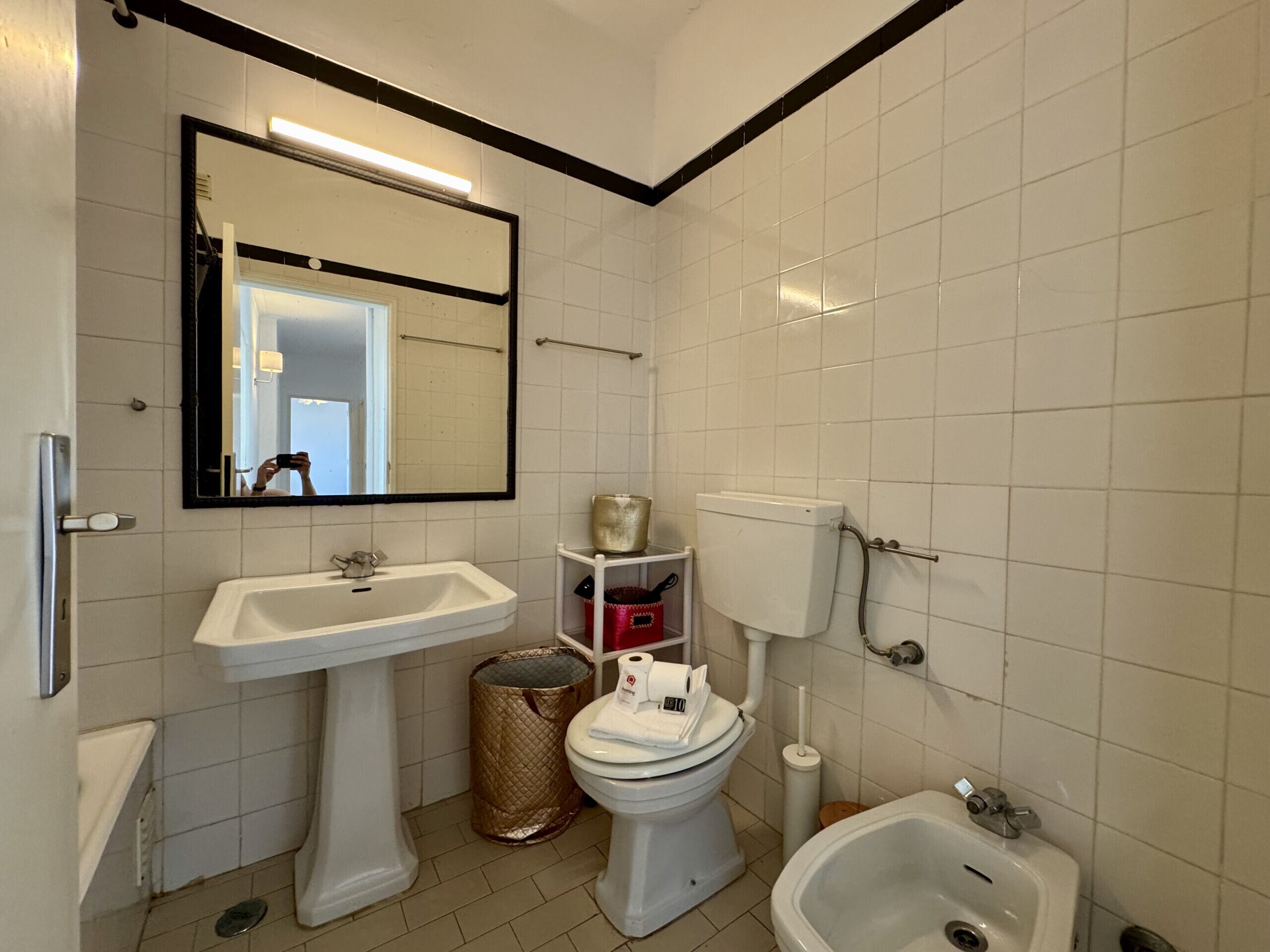 A bathroom with a pedestal sink, toilet, bidet, and a mirror with a black frame.