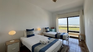 A hotel room with two beds, a nightstand, a lamp, and a view of the landscape. - Praia DA Rocha Twins 5 by Homing (Portimão)