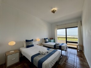 A hotel room with two beds, a nightstand, a lamp, and a view of the landscape. - Praia DA Rocha Twins 5 by Homing (Portimão)