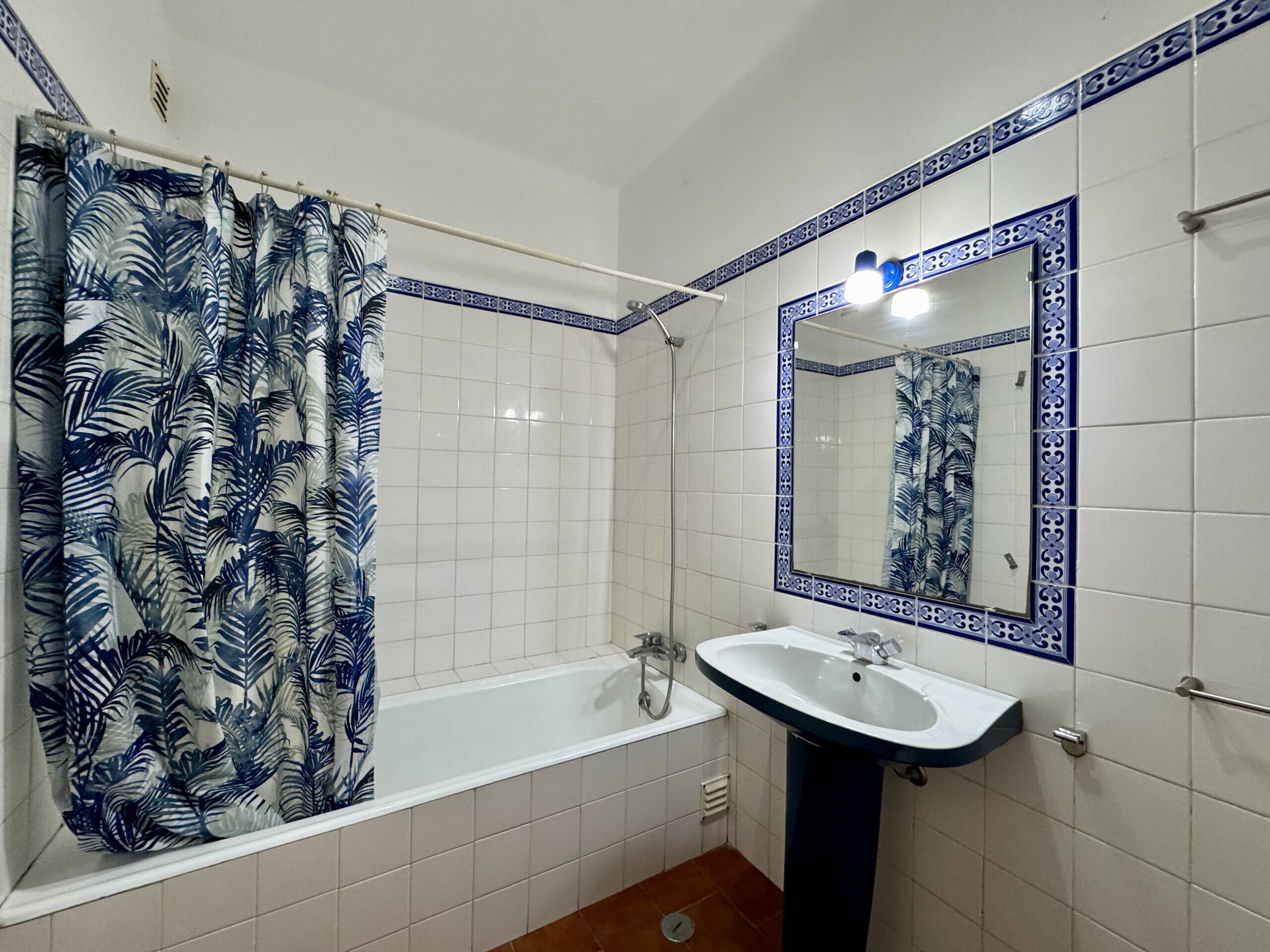 Ein Badezimmer mit einer Badewanne, einem Waschbecken und einem Duschvorhang mit Blättermuster.