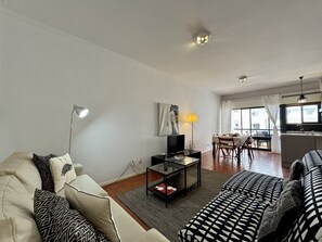 Ein Wohnzimmer mit einer Couch, einem Couchtisch, einem Fernseher und einem Essbereich mit Tisch und Stühlen.