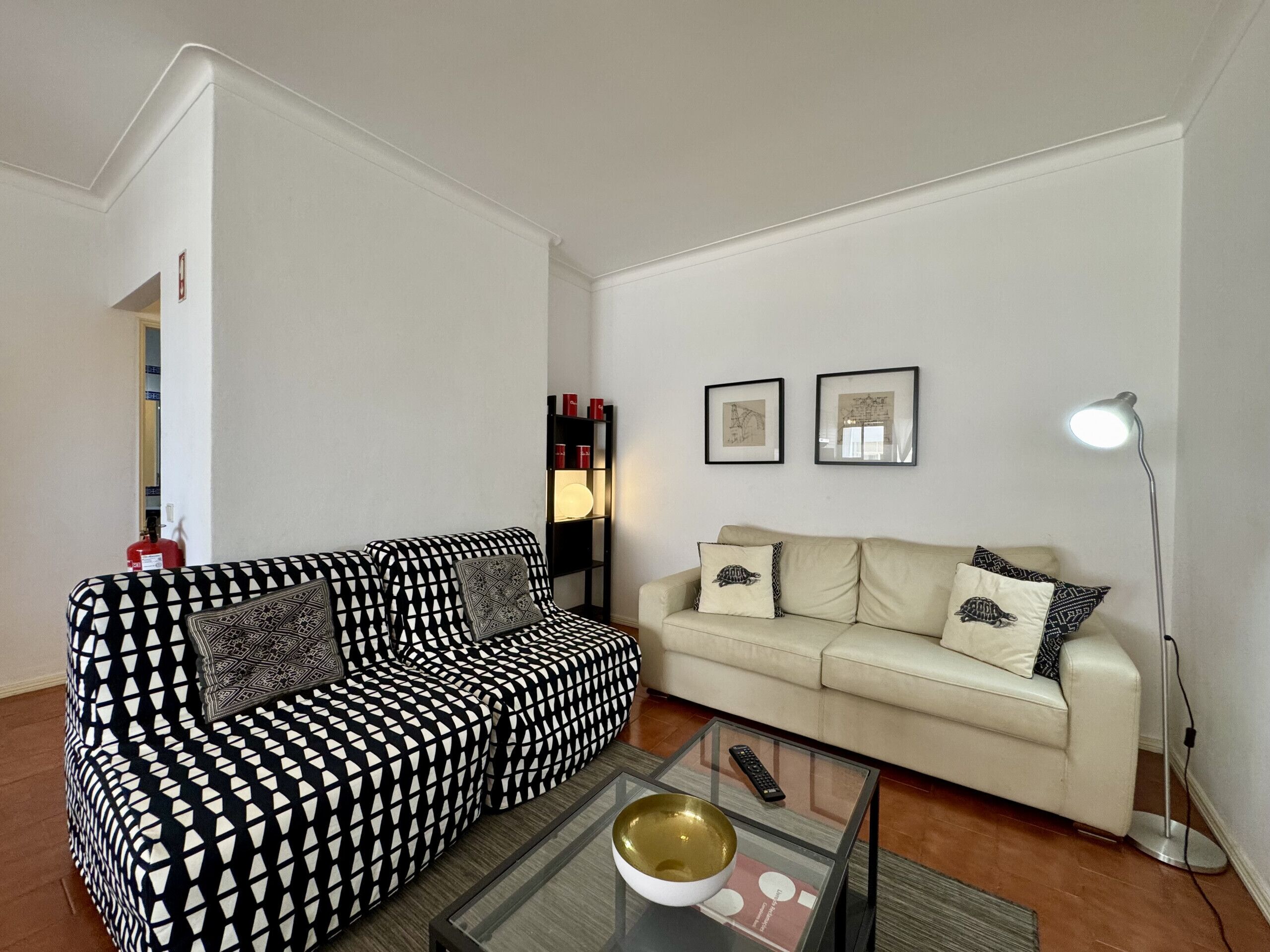 A living room with a patterned sofa, a plain sofa, a coffee table with a bowl, and a floor lamp.
