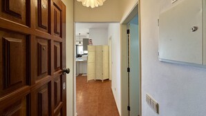 Ein Korridor mit einer Holztür, einer weißen Wand mit einem Notausgangsschild, einem gemusterten Vorhang und einem Küchenbereich im Hintergrund.