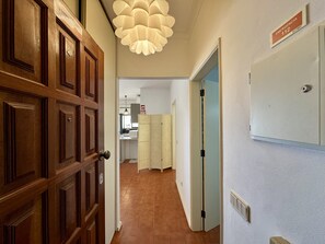 Ein Korridor mit einer Holztür, einer weißen Wand mit einem Notausgangsschild, einem gemusterten Vorhang und einem Küchenbereich im Hintergrund.