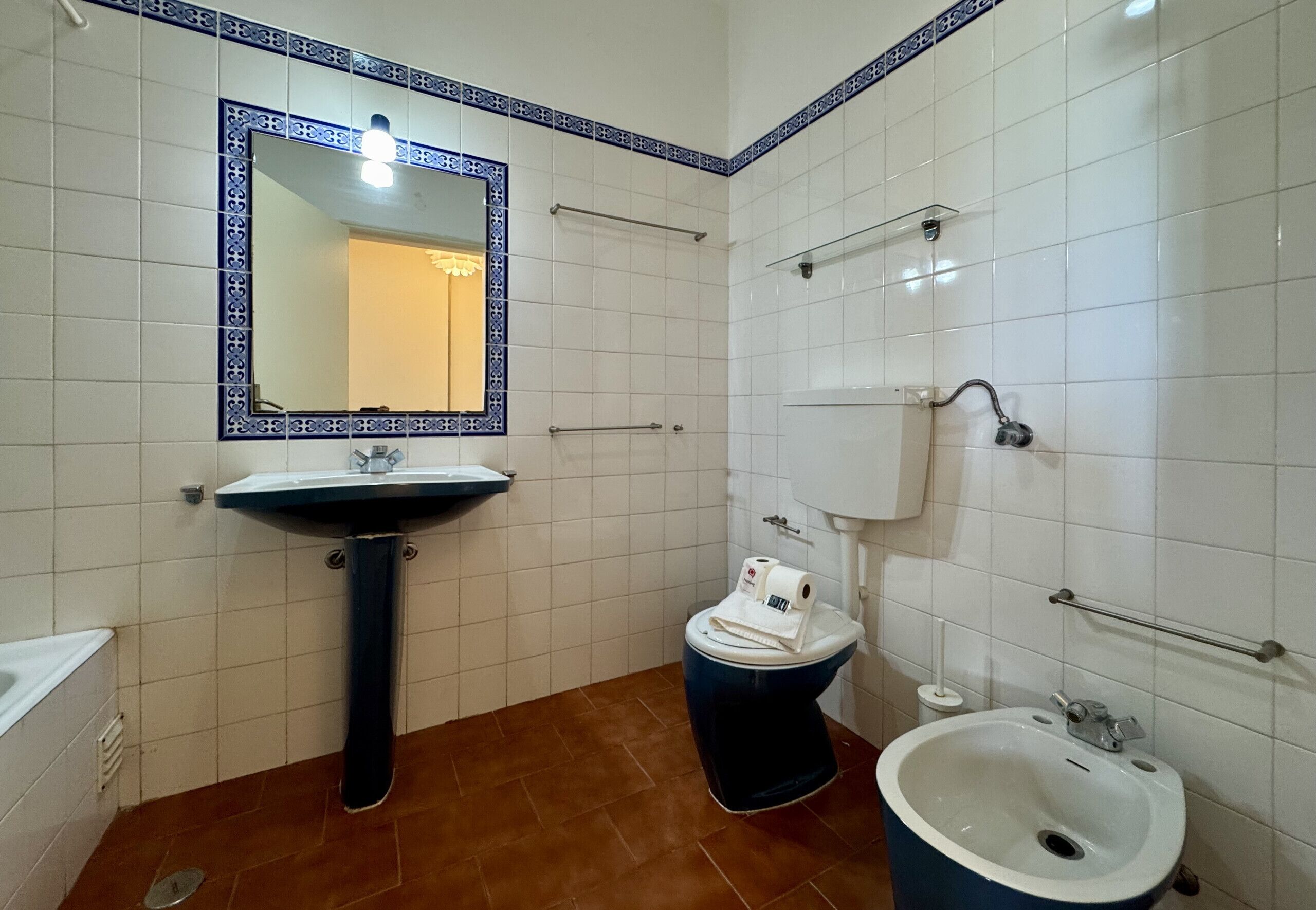 Ein Badezimmer mit einem Waschbecken auf Säule, einer Toilette, einem Bidet und einem Spiegel mit dekorativem Rahmen.