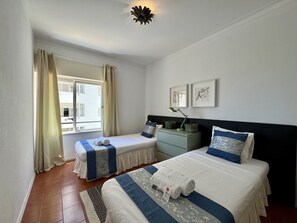 Ein Hotelzimmer mit zwei Betten, einem Nachttisch, einer Lampe und einem Fenster mit Vorhängen.