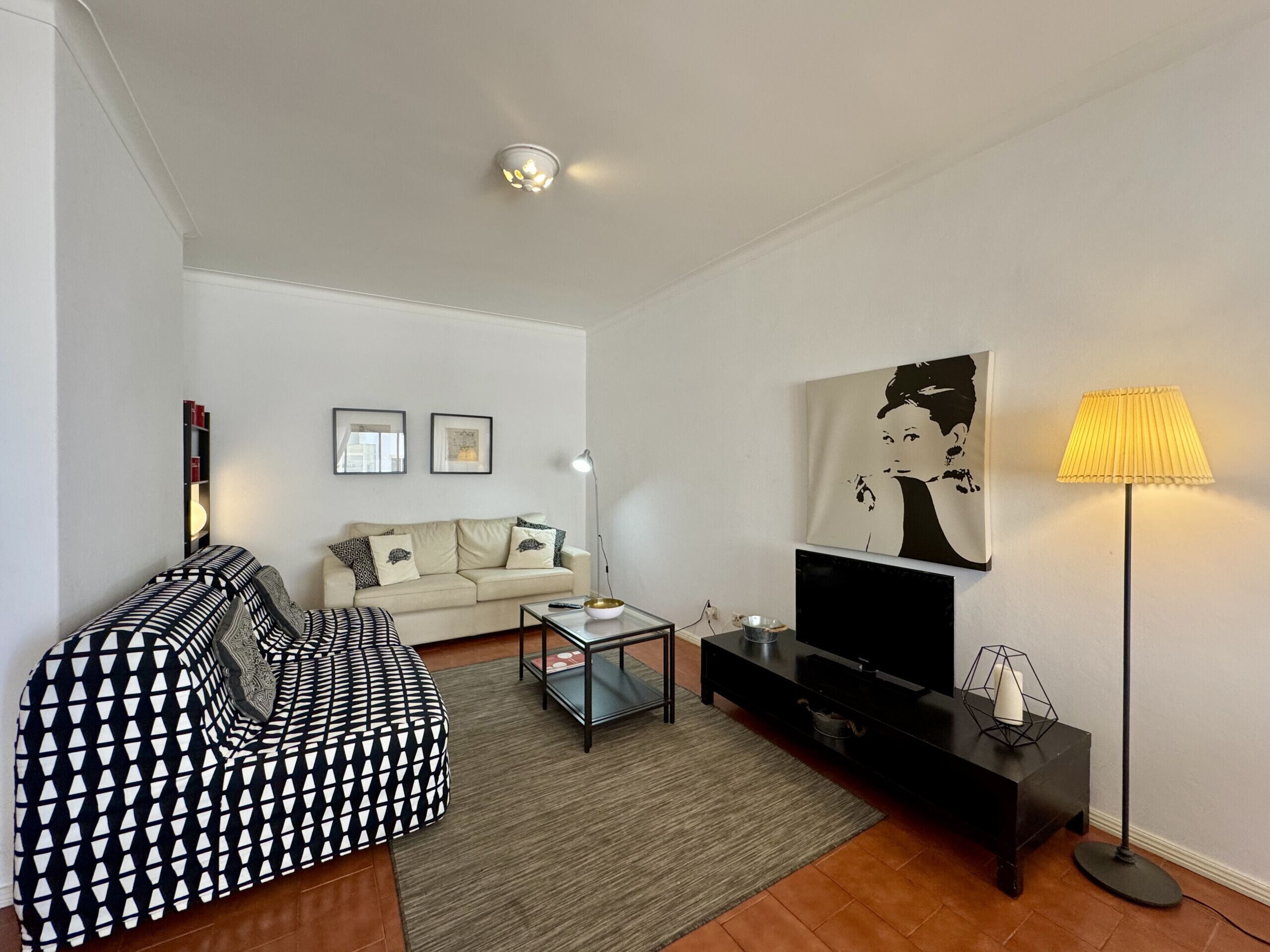 Un salon comprenant un canapé, une table basse, un meuble pour la télévision, une lampe et des œuvres d’art accrochées au mur.