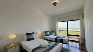Una camera d'albergo con due letti, un comodino, una lampada e vista sul paesaggio.