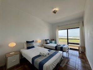 Ein Hotelzimmer mit zwei Betten, einem Nachttisch, einer Lampe und Blick auf die Landschaft.