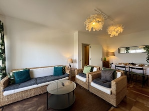 Ein Wohnzimmer mit Rattanmöbeln, einem runden Couchtisch und einem Essbereich mit Tisch für vier Personen.