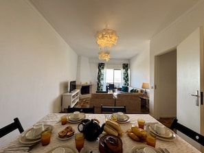 Ein Essbereich mit einem für das Frühstück gedecktem Tisch, einem Kamin und Blick zum Wohnzimmer.