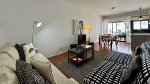 En stue med sofa, sofabord, fjernsyn og et spiseområde med bord og stole.