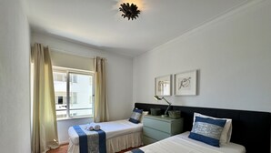 Et hotelværelse med to senge, et natbord, en lampe og et vindue med gardiner.