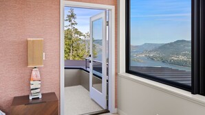 Une pièce avec vue sur un lac et des collines, une porte donnant sur l’extérieur et une lampe sur une table d’appoint.