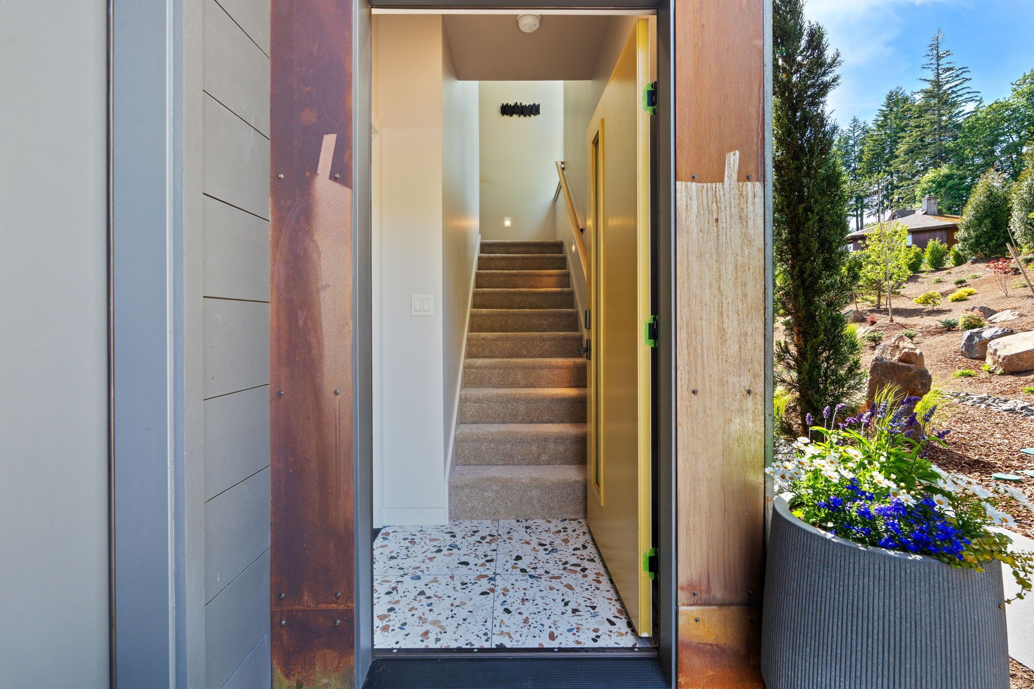Interior moderno com escada que leva a um quarto, porta de madeira e vista para o jardim.