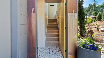 Interior moderno com escada que leva a um quarto, porta de madeira e vista para o jardim.