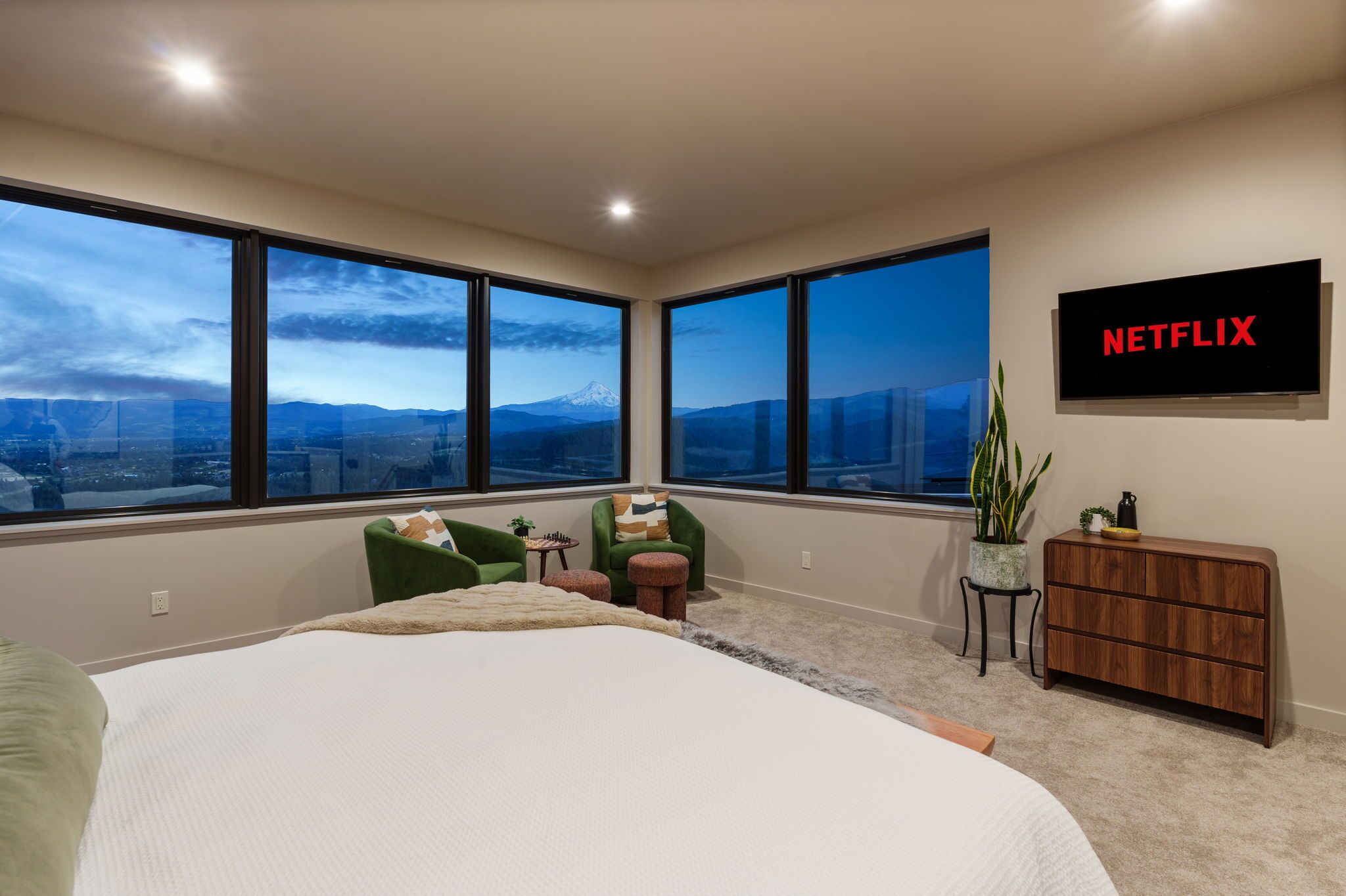 Ein Schlafzimmer mit einem großen Bett, einem an der Wand montierten Fernseher und Bergblick durch große Fenster.