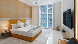 A modern hotel room with a large bed, a flat-screen TV, a large window, and a ceiling light fixture. - Luxury Holiday Home | Spacious & Fully Furnished (Dubai)